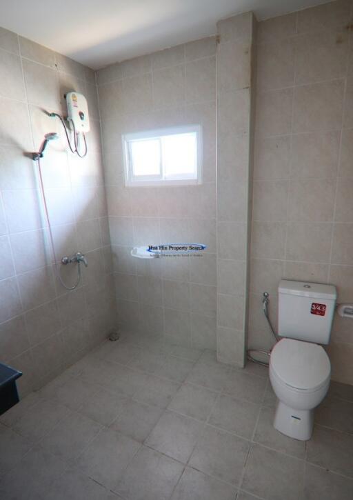 Spacious tiled bathroom with modern fixtures including a shower area, toilet, and electrical water heater
