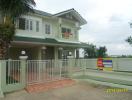 Two-story house with balcony and gated entrance, For Sale sign visible