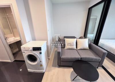 Living area with washing machine, sofa, and a sliding glass door to the bedroom