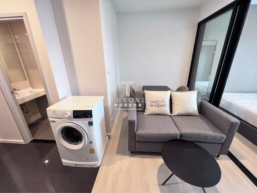 Living area with washing machine, sofa, and a sliding glass door to the bedroom