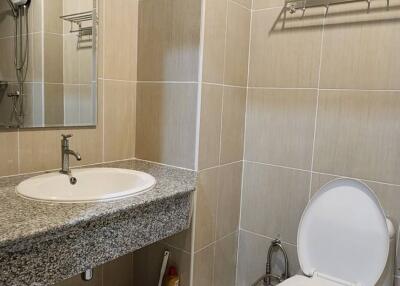 Modern bathroom with gray tiled walls and floor, featuring a wall-mounted sink, toilet, and mirror.