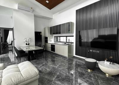Modern living area with open kitchen and dining space, featuring marble flooring, white and gray decor, and a flat-screen TV