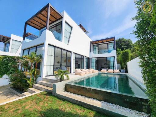 Modern white building with large windows, outdoor seating area, and swimming pool