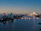 Panoramic evening view of a city skyline with a lit cable-stayed bridge over a river