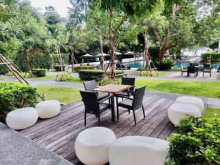 Modern outdoor patio with seating and a view of a lush garden and pool area