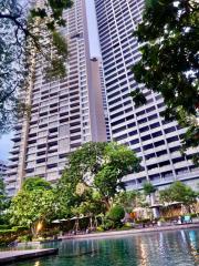 Modern high-rise residential building viewed from a pool area with greenery