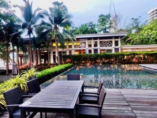 Outdoor patio area with dining table overlooking a pool with palm trees and a building in the background