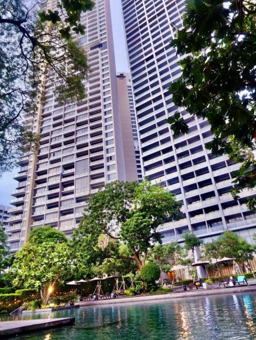 High-rise residential building exterior view with surrounding greenery and pool