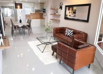 Modern open concept living area with connected kitchen, including a brown leather sofa set, dining table, and kitchen island