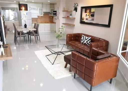 Modern open concept living area with connected kitchen, including a brown leather sofa set, dining table, and kitchen island