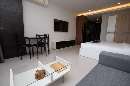 Modern bedroom with integrated living area, including bed, sofa, and flat-screen TV