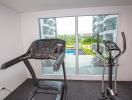 Home exercise room with treadmill and elliptical trainer overlooking a swimming pool