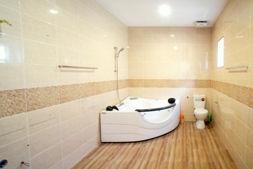 Spacious modern bathroom with a corner jacuzzi tub, toilet, and tiled flooring