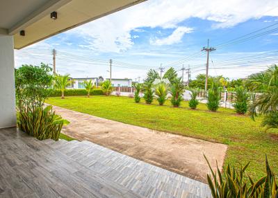 Spacious backyard with green lawn and tropical landscaping viewed from a covered patio