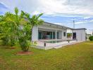 Modern single-story house with a vibrant green lawn and tropical plants