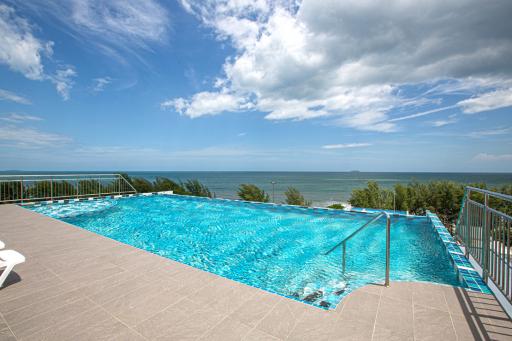 Luxurious infinity pool with sea view and spacious tiled patio under clear blue sky