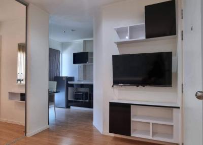 Modern living room interior with flat-screen TV, white shelving units, and open doorway to bedroom