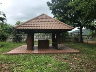 Outdoor wooden gazebo with terracotta tile roof in a green garden setting