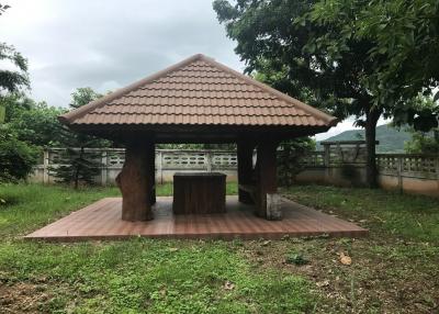 Outdoor wooden gazebo with terracotta tile roof in a green garden setting