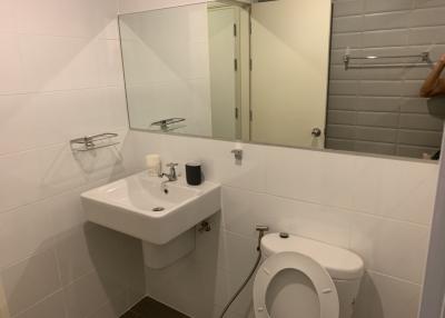 Small bathroom with white tiles, sink, mirror, and toilet