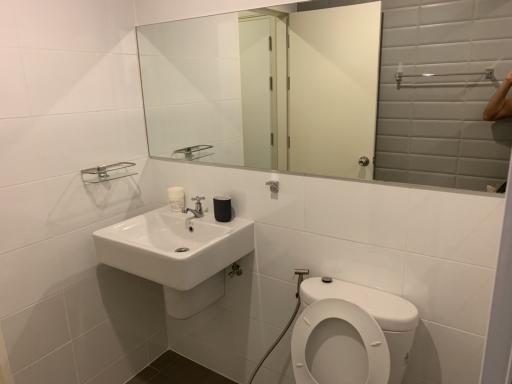 Small bathroom with white tiles, sink, mirror, and toilet