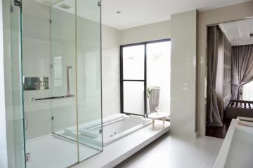 Modern bathroom with glass shower, bathtub, and natural light