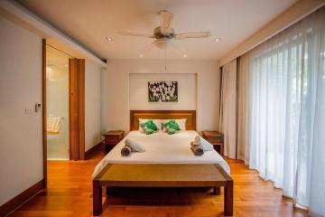 Spacious bedroom with wooden bed and flooring, ceiling fan, and attached bathroom