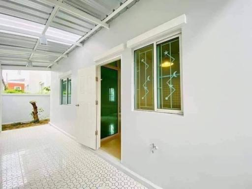 Exterior view of a house with a white facade, green door and windows, and a covered pathway