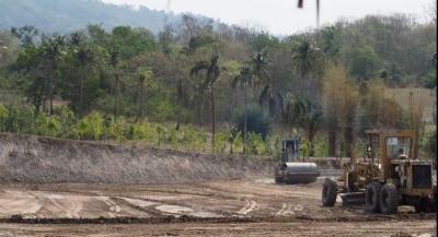 Construction equipment and cleared land at a developing property site with tropical vegetation in the background