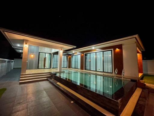 Modern home exterior at night with illuminated facade and swimming pool