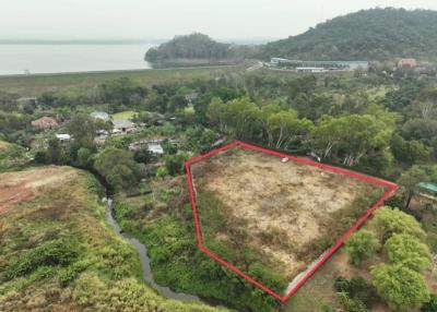 Aerial view of a vacant land plot outlined in red near a water body with green surroundings