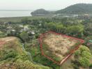 Aerial view of a vacant land plot outlined in red near a water body with green surroundings