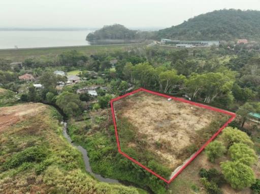 Aerial view of a vacant land plot outlined in red near a water body with green surroundings