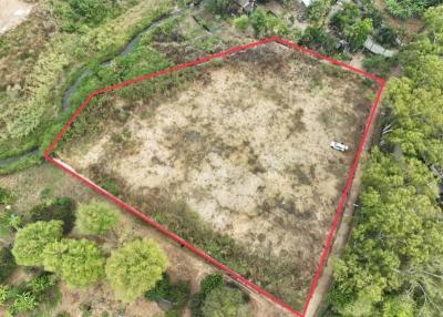 Aerial view of a large vacant land plot outlined in red, with surrounding vegetation