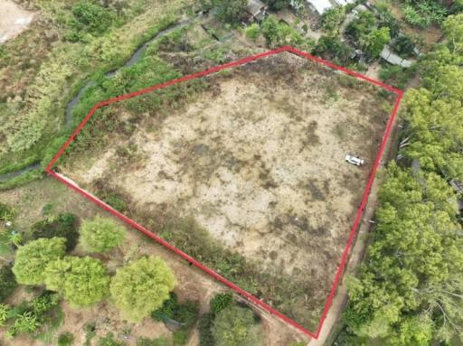 Aerial view of a large vacant land plot outlined in red, with surrounding vegetation