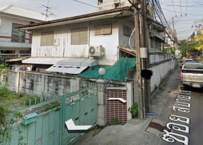 Street view of a residential building with visible air conditioning units and a green fence