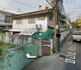 Street view of a residential building with visible air conditioning units and a green fence