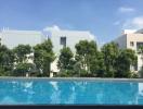 Sparkling outdoor swimming pool with modern buildings and lush greenery in the background