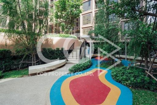 Entrance of a modern apartment building with lush greenery and a colorful pathway