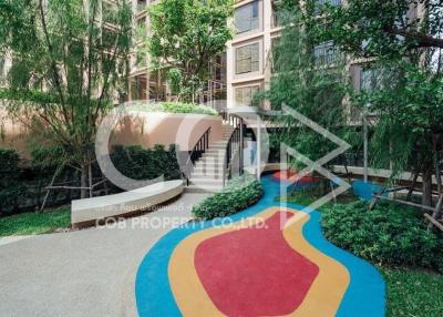 Entrance of a modern apartment building with lush greenery and a colorful pathway