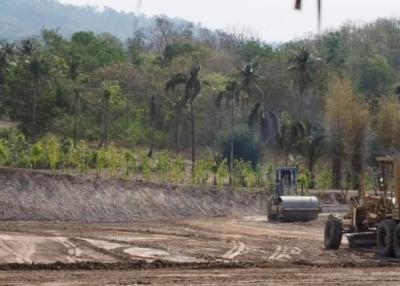 Construction vehicles and land clearing in progress at a site with tropical vegetation in the background