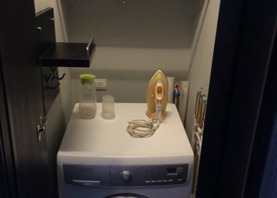 Compact laundry room with washing machine, shelves, and iron