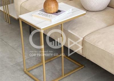 Elegant living room detail showing a modern gold accent side table with decorative vase and book