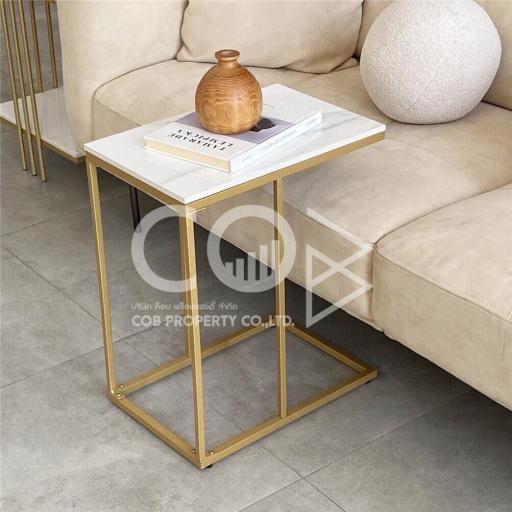 Elegant living room detail showing a modern gold accent side table with decorative vase and book