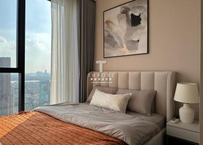 Elegant bedroom with a large window offering a city view, featuring a comfy bed with stylish bedding and a prominent art piece on the wall.