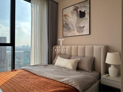 Elegant bedroom with a large window offering a city view, featuring a comfy bed with stylish bedding and a prominent art piece on the wall.