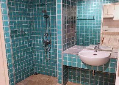 Modern bathroom with teal tiles, glass shower, and beige flooring