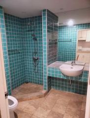 Modern bathroom with teal tiles, glass shower, and beige flooring