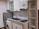 Compact kitchen with white cabinets, washing machine, and built-in sink