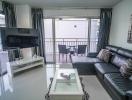 Modern living room interior with large sofa and flat-screen TV leading to a balcony